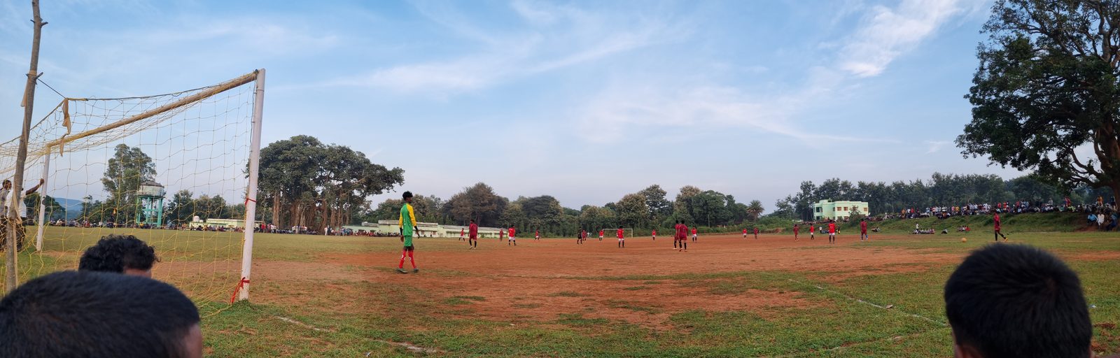 Villagers watching a football match on the red earth ground