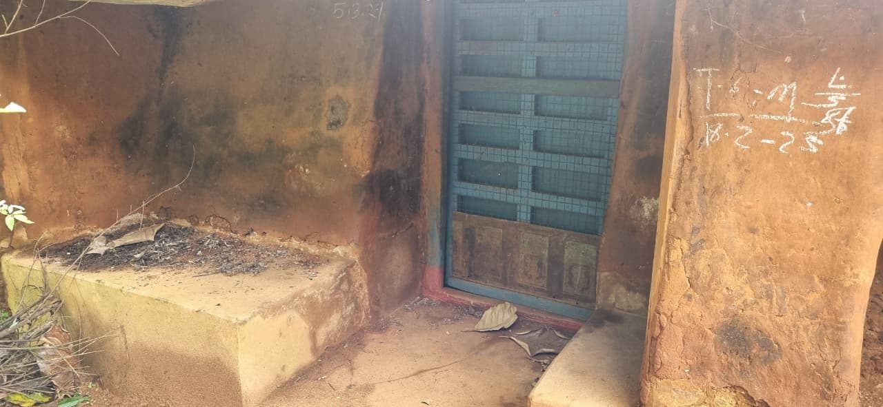 Blue metal door set in a mud-plastered wall, chalk writing and dates on the laterite beside it, a low bench of packed earth to the left
