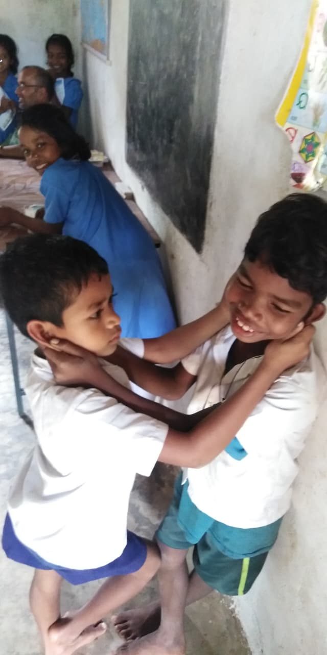 Two boys holding each other by the ears and laughing in a classroom, blackboard behind