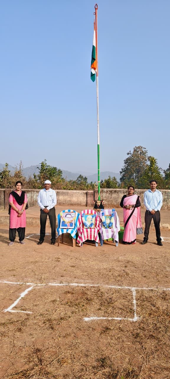Five teachers standing either side of a table of framed portraits beneath a flagpole on a school ground